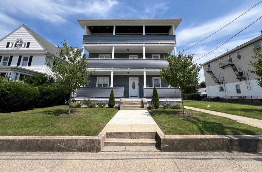 Three-story gray house with balconies and a well-kept front yard.