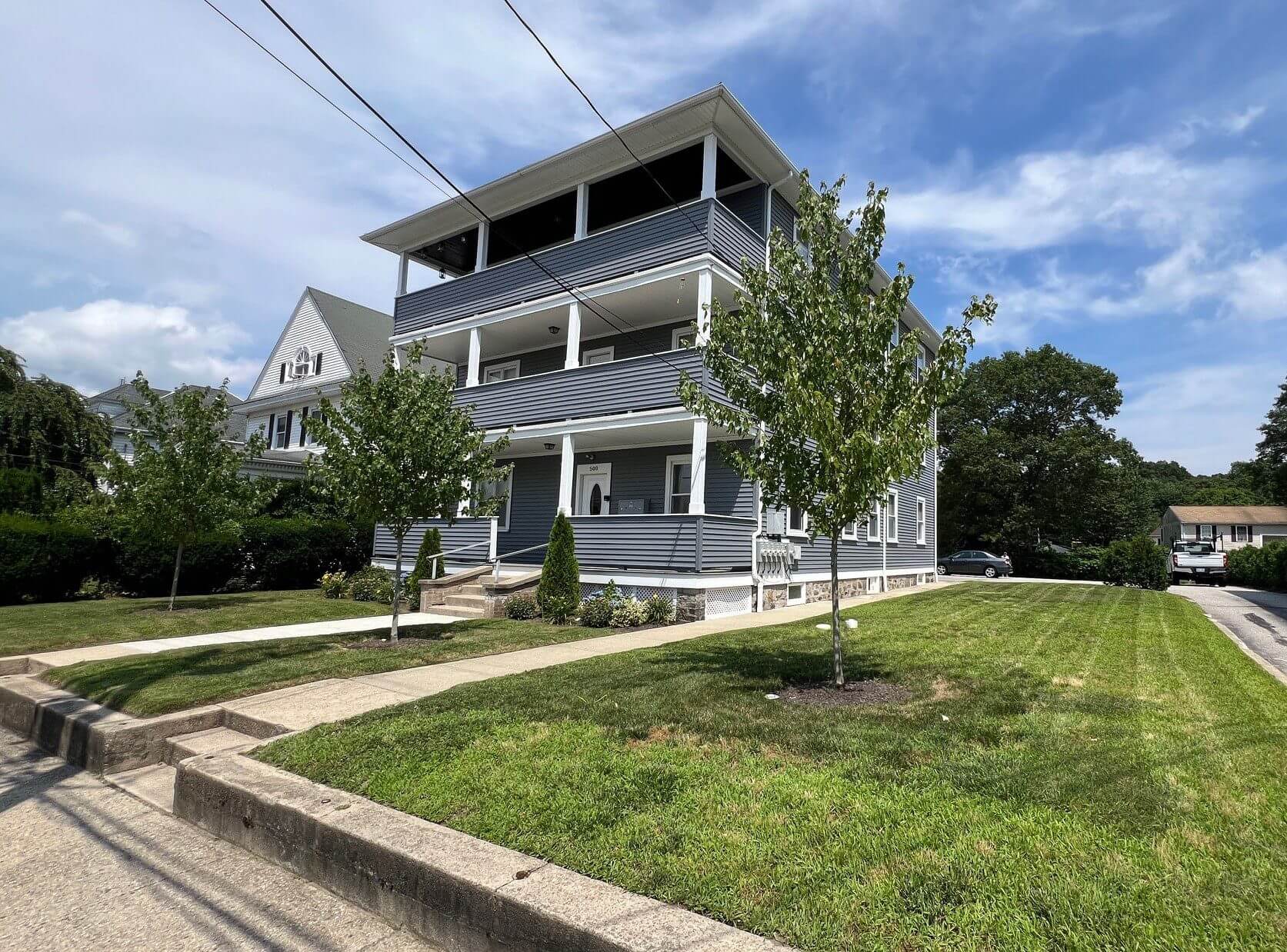 Three-story gray house with balconies and a green lawn under a blue sky.