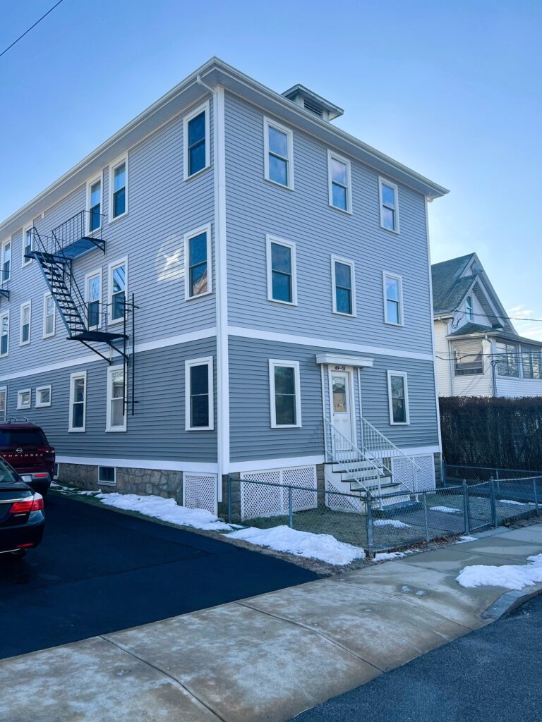 Three-story gray apartment building with fire escape.